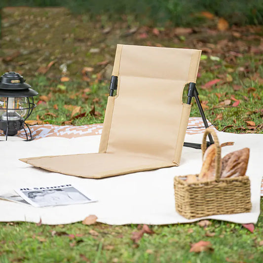 Beige folding chair on a picnic blanket with a basket and lantern in an outdoor setting